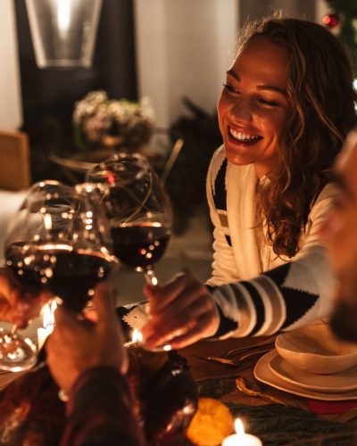 Photo of happy cute people drinking wine and smiling while having Christmas dinner in cozy room